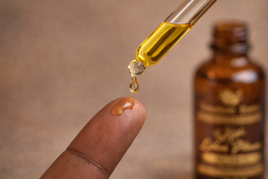 Dropper with yellow liquid being dripped onto a finger, with a brown bottle in the background.